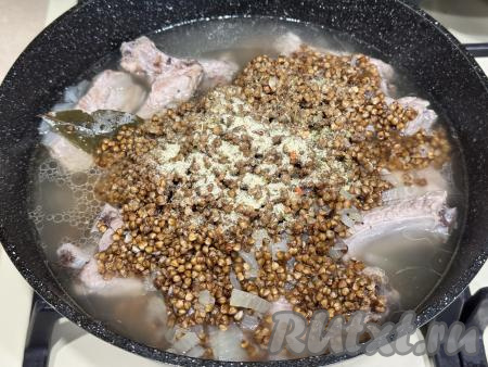 В сковороду со свиными рёбрышками и бульоном выложить подготовленную гречку, добавить соль по вкусу.