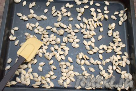 Противень с тыквенными семечками поставить в духовку, разогретую до 150 градусов. Сушить тыквенные семечки 10 минут, затем вынуть противень из духовки. После первой сушки семечки пристанут к противню, их следует отделить от поверхности противня лопаткой и как следует перемешать.