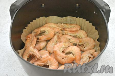 Чашу аэрогриля застилаем пергаментной бумагой. Выкладываем креветки, замаринованные с чесноком.