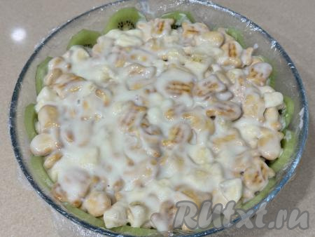 Получившуюся массу из печенья, крема и сметаны выложить в миску с киви, слегка утрамбовать, разровнять, накрыть краями плёнки, свисающими с краёв миски.&nbsp;