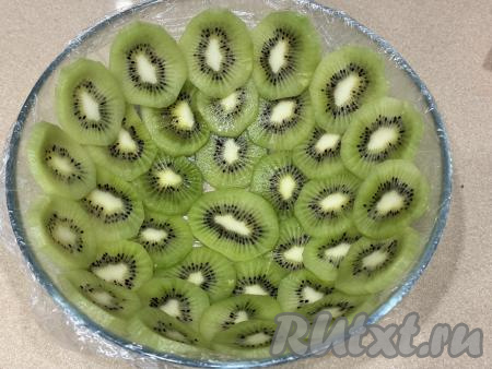 Взять миску (я взяла миску диаметром 20 сантиметров), выстелить дно и бока миски пищевой плёнкой так, чтобы края плёнки свисали с краёв миски. Киви почистить и нарезать на достаточно тонкие кружочки. Дно и бока миски выложить кружочками киви, выкладывая киви&nbsp;немного внахлёст.