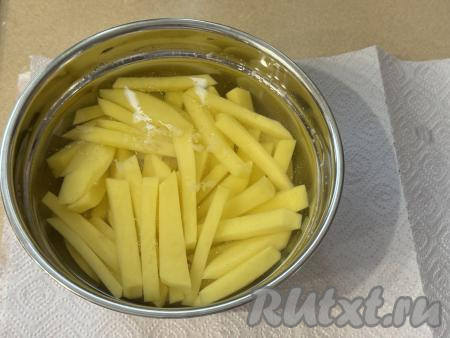 Картошку, нарезанную на брусочки, выложить в глубокую миску, залить полностью холодной водой и оставить на 20 минут. Благодаря замачиванию в воде, из картофеля выйдет крахмал и он будет меньше приставать к решётке в процессе запекания в аэрогриле.