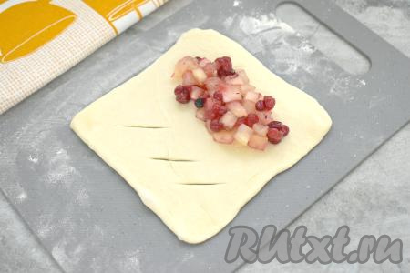 Яблочно-брусничную начинку зрительно разделить на 4 равных части (по количеству слоек, которое мы будем формировать). Каждую часть теста раскатать до толщины примерно 2-3 миллиметра. Получится квадратная заготовка для слойки. Визуально поделить квадрат на 2 равных части. На одной части квадрата из теста сделать 3 надреза, как на фото. На сторону без надрезов выложить одну часть яблочно-брусничной начинки, отступая от краёв теста 1-1,5 сантиметра.