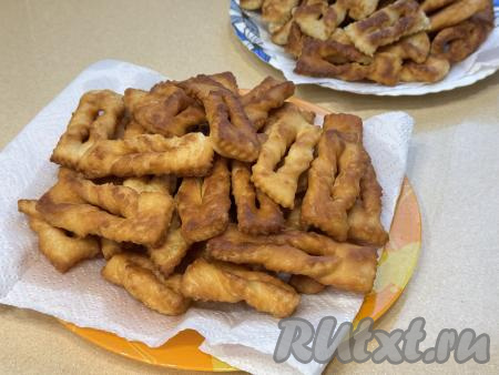 Жареный хворост переложить со сковороды на тарелку, застеленную бумажным полотенцем, чтобы удалить излишки масла. Постепенно пожарить все заготовки дрожжевого хвороста, не забывая подливать в сковороду масло по мере необходимости.