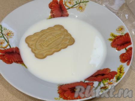 Предварительно пластиковый лоток (или форму) выстелить пищевой плёнкой так, чтобы края плёнки свисали с краёв лотка. Обмакнуть печенье с двух сторон в молоко.&nbsp;