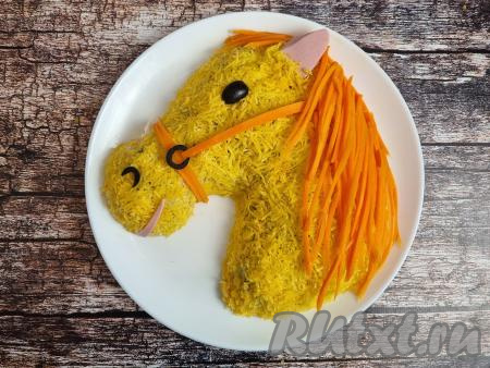 Вырезать ухо и рот лошади из колбасы, разместить на голове лошади. Ноздрю, глаз и кольцо сбруи сделать из маслин, расположить на голове лошадки. Сбрую и гриву лошади сформировать из морковки.