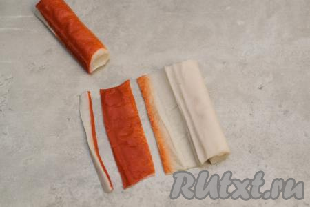Крабовые палочки, если они заморожены, нужно заранее разморозить. Каждую палочку освободить от слюды, немного раскрутить. Отрезать красную часть каждой палочки, отложить в сторону. Красная часть крабовых палочек понадобится для оформления новогоднего салата "Лошадь".