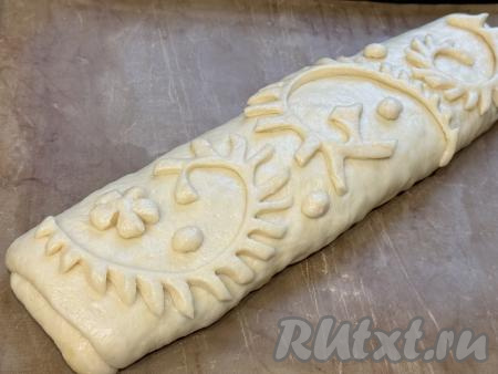 Перевернуть рулет швом вниз&nbsp;и переложить на противень, застеленный ковриком (или пергаментом) для выпечки. Оставить рулет на 15 минут под полотенцем. Из отложенного кусочка теста сформировать узоры для украшения и выложить поверх рулета.