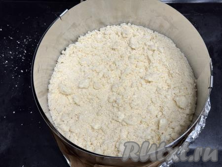 В разъёмную форму для выпечки диаметром 24 сантиметра насыпать 1/2 песочного теста-крошки, слегка утрамбовать. Я в качестве формы решила использовать кулинарное кольцо, сформировав его дно из пергаментной бумаги и фольги, сложенной в несколько слоёв. Затем получившуюся форму поставила на противень и только после этого выложила половину теста-крошки.