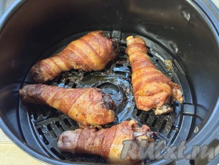 Поставить чашу с ножками в беконе в аэрогриль, установить температуру 160 градусов, время - 30 минут. Через 15 минут с момента начала запекания ножки нужно перевернуть и готовить оставшиеся 15 минут. Затем снова ножки перевернуть, уменьшить температуру до 140 градусов и запекать 15 минут (до готовности мяса). Для того чтобы проверить готовность, нужно проколоть куриную ножку вилкой, если выделяется прозрачный сок без примесей крови, значит мясо готово.&nbsp;