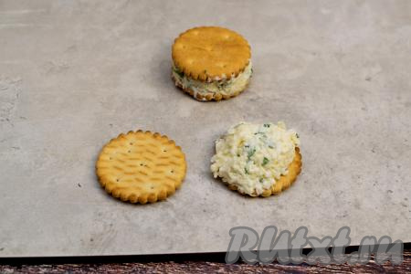 На крекер выложить часть сырно-яичной начинки, сверху положить второй крекер, слегка прижать получившийся бутерброд на крекерах. Для этой закуски лучше всего подойдут солёные крекеры любой формы и размера. У меня были круглые сырные крекеры.