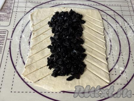 Нарезать чернослив на мелкие кусочки, выложить ровным слоем на середину теста, отступая от более узких краёв прямоугольника по 1,5-2 сантиметра и не заходя на часть теста, нарезанную на полоски.&nbsp;