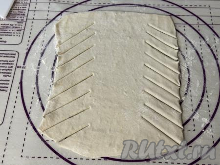 Более длинные края получившегося прямоугольника нарезать на полоски шириной примерно 1,5 сантиметра, делая полоски немного под наклоном, как на фото, оставляя середину раскатанного пласта без разрезов.&nbsp;