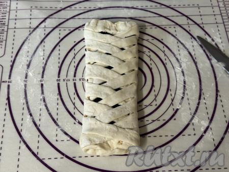 Поверх чернослива, начиная с подвёрнутого края, приступить к заворачиванию полосок теста с двух сторон внахлёст, формируя косу, как на фото. Край каждой завёрнутой полоски нужно прижимать пальцами к тесту.&nbsp;