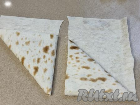 Начиная с подвёрнутого края полоски, подворачивать лаваш дальше, формируя треугольный конвертик. Оставшийся край лаваша завернуть внутрь треугольника.