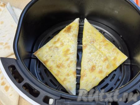 В небольшой ёмкости взбить до однородности яичный желток. Перед запеканием смазать верх треугольника из лаваша взбитым желтком (смазывать нужно столько треугольников, сколько у вас одновременно поместятся в чашу аэрогриля). По желанию можно присыпать треугольники кунжутом (или маком).&nbsp;Выложить на решётку в чашу аэрогриля 2 треугольники из лаваша с начинкой из творога и сыра.