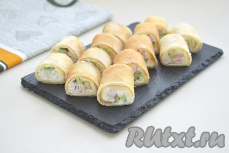 Блин, начиная со стороны с начинкой, сворачиваем в плотный рулет. Аналогично формируем ещё 5 рулетов, используя все блины и всю начинку из крабовых палочек и огурцов. Острым ножом каждый блинный рулет нарезаем на рулетики шириной около 2,5 сантиметров.