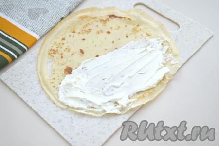 Даём блинчикам немного остыть. Заранее размораживаем крабовые палочки. Огурец моем, обрезаем кончики с двух сторон. В небольшой ёмкости смешиваем творожный сыр и майонез. Раскладываем на доске первый блин. Одну половину блина, немного отступая от краёв, смазываем 1,5 столовыми ложками творожного сыра, смешанного с майонезом.&nbsp;