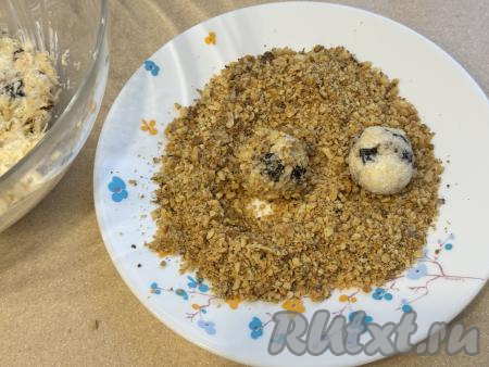 Измельчённые грецкие орехи насыпать на тарелку. Периодически смачивая руки водой, из массы, получившейся из сыра и чернослива, сформировать&nbsp;шарики размером чуть меньше, чем грецкий орех. Обвалять каждый шарик в ореховой крошке со всех сторон.