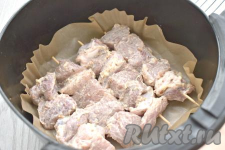 За 15 минут до начала приготовления шашлыков в аэрогриле деревянные шпажки выкладываем в достаточно глубокую посуду, заливаем полностью холодной водой. Благодаря замачиванию, шпажки не будут тлеть в процессе приготовления шашлыков. Затем кусочки свинины, замаринованные в майонезе, нанизываем на подготовленные шпажки и выкладываем в чашу аэрогриля, заранее застеленную пергаментом. Лук нам больше не понадобится. У меня получились 4 шашлычка.