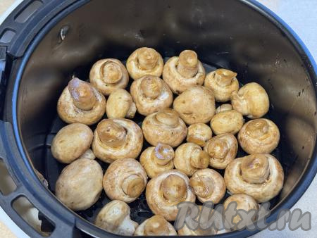 По прошествии часа шампиньоны, замаринованные в соевом соусе, выложить в чашу аэрогриля на решётку в один слой ножками вверх. Отправить чашу в аэрогриль, выставить температуру 180 градусов, время - 15 минут.