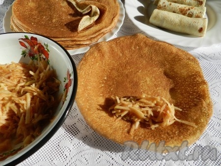 Взять один блин, немного отступив от его края, выложить примерно 1 столовую ложку с горкой начинки из свежих яблок, смешанных с сахаром. Затем подвернуть вначале боковые края блина на начинку и, начиная со стороны с начинкой, свернуть блин в рулет. Постепенно нафаршировать яблоками все блинчики.