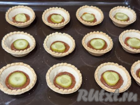 Огурец нарезать на кружочки. Выложить по кружочку огурца в тарталетку поверх кетчупа.&nbsp;