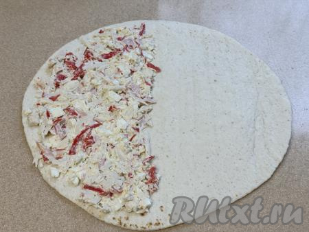 На одну половину тортильи, немного отступая от краёв лепёшки, выложить 1/4 часть начинки из крабовых палочек и яиц, равномерно распределить начинку по половине тартильи.