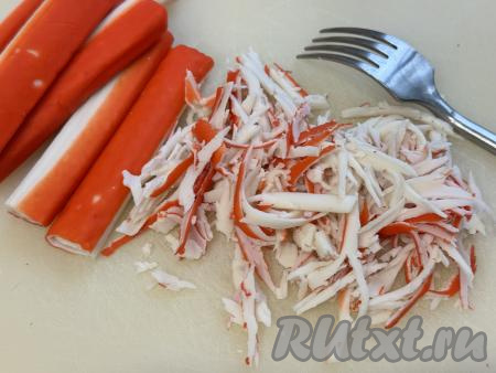 Крабовые палочки вынуть из упаковки, тонко нарезать или с помощью вилки разделить на тонкие полоски.