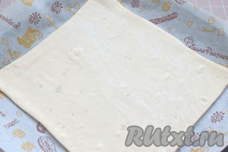 На рабочую поверхность, слегка присыпанную мукой, выкладываем первый размороженный пласт слоёного теста, раскатываем его скалкой в квадрат со стороной 25 сантиметров. Раскатанное тесто перекладываем на противень, заранее застеленный пергаментом.&nbsp;
