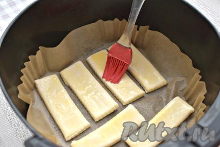 Чашу аэрогриля застилаем пергаментом, выкладываем полоски из слоёного теста в один слой. У меня поместились только 6 полосок, поэтому я выпекала язычки в два захода. Полоски из теста смазываем взбитым яйцом.