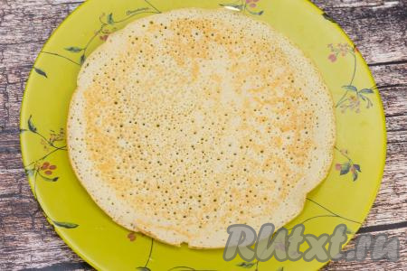 Готовый блин переложить на плоскую тарелку. Перемешивая тесто перед жаркой очередного блина и смазывая сковородку маслом только по мере необходимости, постепенно пожарить все блинчики, складывая их один на другой на тарелку. Я обычно после жарки первого блина сковороду маслом не смазываю, потому что масла вполне достаточно в тесте, но многое безусловно зависит от качества покрытия сковородки, на которой вы готовите.