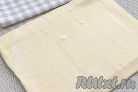Размороженный пласт слоёного теста выкладываем на стол, присыпанный мукой, раскатываем его в квадрат толщиной примерно 3 миллиметра.