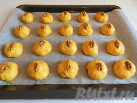 Противень застелить бумагой для выпечки. Руками, смоченными водой, скатать из тыквенного теста шарики размером чуть больше грецкого ореха, выкладывать их на противень на расстоянии друг от друга. Я сформировала 20 заготовок печенья. На каждое тыквенное печенье выложить по кусочку грецкого ореха, слегка вдавить его в тесто.