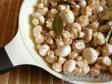 Шампиньоны выложить в глубокую сковороду (или сотейник), добавить растительное масло, яблочный уксус, соль, сахар, смесь перцев, зёрна горчицы, пропущенный через пресс чеснок, сушёный орегано и лавровые листья, перемешать, накрыть крышкой и поставить на средний огонь.