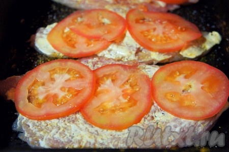 Тем временем духовку разогреть до 180-200 градусов. Помидор вымыть и тонко нарезать. Сыр натереть на мелкой тёрке. Куриные грудки смазать майонезом, выложить нарезанные помидоры.
