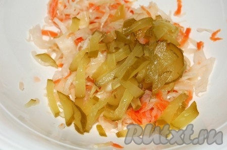 Добавить нарезанные соленые огурцы в миску с капустой.