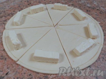 На край каждого сектора положить по 1/3 кусочка сыра Kiri, затем завернуть каждый сектор из дрожжевого слоеного теста в рогалик от края к центру.