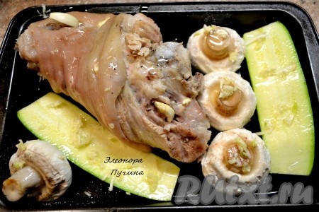 Далее достаем рульку, чеснок нарезаем пластинками и шпигуем им рульку. Выкладываем на противень свиную рульку, кабачок, грибы и ставим в духовку подрумяниться при температуре 220 градусов на 15-20 минут.
