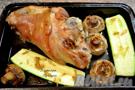 Далее достаем рульку, чеснок нарезаем пластинками и шпигуем им рульку. Выкладываем на противень свиную рульку, кабачок, грибы и ставим в духовку подрумяниться при температуре 220 градусов на 15-20 минут.