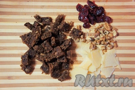 Тем временем клюкву замочить на 5 минут в кипятке, затем достать, обсушить. Грецкие орешки произвольно нарезать, слегка подсушить на сухой сковороде, дать им остыть. Хлеб нарезать "кубиком", слегка обжарить на оливковом масле, выложить на бумажное полотенце, чтобы удалить излишки масла, дать сухарикам остыть. Приготовить пармезан.
