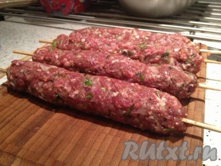 Теперь берем в руки фарш и с силой кидаем его о рабочую поверхность и так до тех пор, пока фарш не станет упругим и клейким (минут 10-15). Оборачиваем деревянные шпажки фаршем и жарим на среднем огне с 4 сторон до зарумянивания.