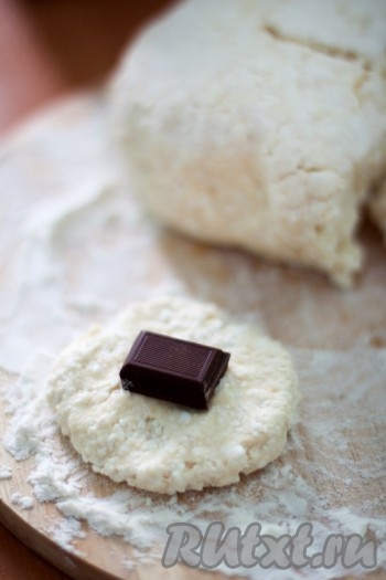 Тесто разделите на кусочки, сделав из них маленькие лепешки, и вложите в центр каждой по одной дольке шоколада. Края защипните, сформировав круглый сырник, и обваляйте в сухарях.
