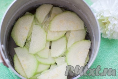 Кабачки нашинкуйте тонкими полукружками. Сложите в сотейник, залейте кипящей водой и поставьте на маленький огонь на 3-4 минуты. Откиньте на дуршлаг, чтобы стекла вода. Нарежьте мелко лук и обжарьте на оливковом масле до золотистости. Измельчите чеснок.