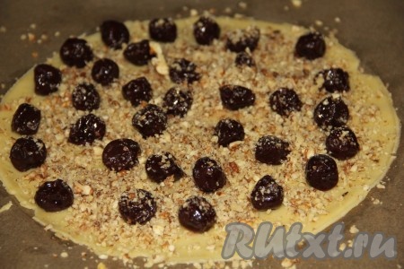 Отдохнувшее тесто достаем и приступаем к выпеканию коржей. На выходе у нас будет три коржа, начинку можете визуально разделить тоже на три части.&nbsp;Для приготовления одного коржа раскатываем один кусочек теста диаметром в 24-26 сантиметров, выкладываем его на противень. Сверху посыпаем его орехами и выкладываем вишню.
