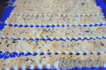 Противень застелить пергаментной бумагой или силиконовым ковриком, выложить сырные полоски на противень. Смажьте их взбитым яйцом, посыпьте кунжутом и оставшимся сыром.
