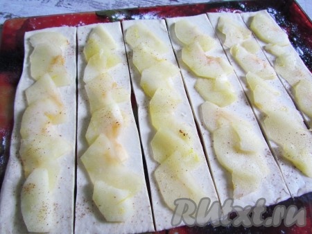 Разрезать раскатанный пласт теста вдоль на полоски шириной ~5 см. Выложить на тесто яблочные ломтики, присыпать корицей.