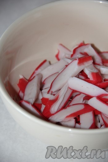 Если крабовые палочки заморожены, тогда их нужно полностью разморозить при комнатной температуре. Нарезать крабовые палочки соломкой и выложить в салатник.