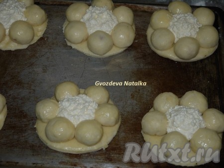 Для большего удобства основу можно сразу разложить на противне, а затем раскладывать шарики с вишней. После того как все шарики будут разложены на основы, смазать их взбитым яйцом. В серединку нашего цветочка выложить по 2 столовые ложки творожной массы.
