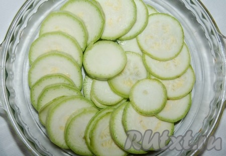 Молодой свежий кабачок помыть, обсушить и нарезать тонкими ломтиками. В форму для запекания налить оливковое масло и выложить ломтики кабачков.